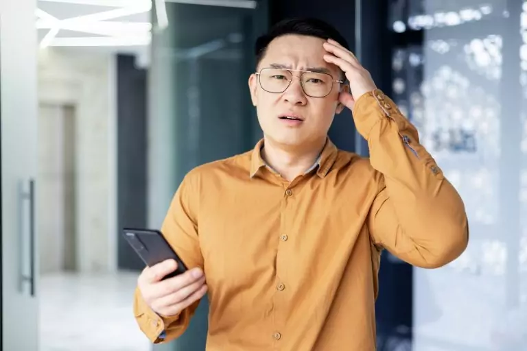 Unzufriedener asiatischer Mann mit Handy im Büro – MakeMore App Best Practices
